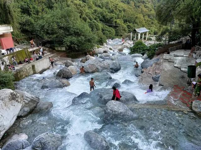Pilgrims bathing in the holy river along the Vaishno Devi Yatra route, surrounded by mountains and natural scenery, reflecting spiritual cleansing and devotion.